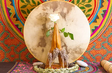 Hands in praying position holding white rose in front of moon and colourful backdrop